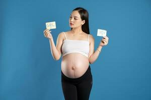 Porträt von schwanger asiatisch Frau, isoliert auf Blau Hintergrund foto