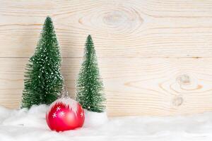 zwei immergrüne Tannen und roter Ball, schneebedeckte Weihnachtskomposition, Holzhintergrund, Kopierraum foto
