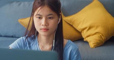 junge asiatische Mädchen Teenager mit Freizeitkleidung Kopfhörer verwenden Laptop-Computer online lernen Vorlesungsnotizbuch im Wohnzimmer im Haus schreiben. Isolieren Sie das Online-E-Learning-Konzept für die Coronavirus-Pandemie. foto