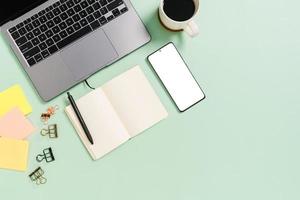 kreatives flaches Laienfoto des Arbeitsplatzschreibtisches. Schreibtisch von oben mit Laptop, Kaffeetasse und offenem schwarzen Notizbuch auf pastellgrünem Hintergrund. Draufsichtmodell mit Kopienraumfotografie.