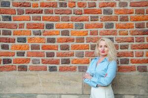 ein erfolgreich Geschäft Frau steht in der Nähe von ein rot Backstein Mauer auf das Straße. ein Frau gekleidet im Weiß Hose und ein Blau Shirt. Kopieren Raum. foto