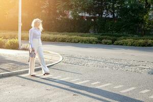 ein ziemlich jung Frau Kreuzung das Straße, halten ein Tasche im ihr Hände. ein warm Sommer- Abend. foto