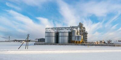 modern Agro-Verarbeitung Pflanze zum wird bearbeitet und Silos zum Trocknen Reinigung und Lager von landwirtschaftlich Produkte, Mehl, Getreide und Korn im Schnee von Winter Feld foto