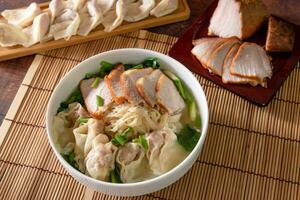 oben oben Wonton Suppe im Schüssel mit geröstet Schweinefleisch und Gemüse, asiatisch Essen Stil zum Speisekarte und Hintergrund foto