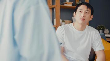 Junge asiatische Ärztin mit digitaler Tablette, die gute Gesundheitstestnachrichten mit glücklichen männlichen Patienten teilt, sitzt auf der Couch im Haus. Krankenversicherung, besuchen Sie den Patienten zu Hause Konzept.