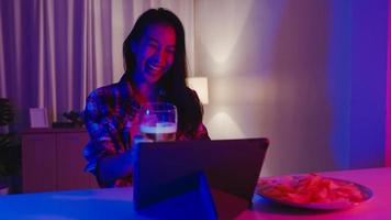 junge asiatische Dame, die Bier trinkt und Spaß hat, glücklicher Moment, Disco-Neon-Nacht-Party-Event, Online-Feier per Videoanruf im Wohnzimmer zu Hause. soziale Distanzierung, Quarantäne zur Coronavirus-Prävention. foto