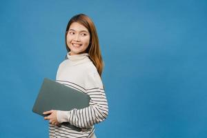 junge asiatische Dame hält Laptop mit positivem Ausdruck, lächelt breit, in Freizeitkleidung gekleidet, fühlt sich glücklich und steht einzeln auf blauem Hintergrund. glückliche entzückende frohe frau freut sich über erfolg.