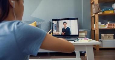 Nahaufnahme junges asiatisches Mädchen mit Freizeitkleidung Kopfhörer verwenden Computer-Laptop-Videoanruf online lernen mit Tutor im Wohnzimmer im Haus. Isolieren Sie das Online-E-Learning-Konzept für die Coronavirus-Pandemie. foto