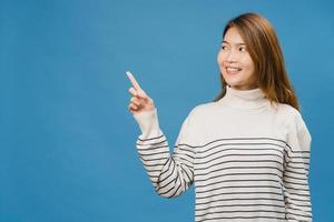Porträt einer jungen asiatischen Dame, die mit fröhlichem Ausdruck lächelt, zeigt etwas Erstaunliches an leeren Stellen in Freizeitkleidung und steht einzeln auf blauem Hintergrund. Gesichtsausdruck Konzept. foto