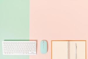 kreatives flaches Laienfoto des Arbeitsplatzschreibtisches. Schreibtisch von oben mit Tastatur, Maus und offenem Mockup-Schwarz-Notizbuch auf pastellgrünem rosafarbenem Hintergrund. Draufsichtmodell mit Kopienraumfotografie. foto