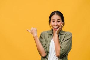 Porträt einer jungen asiatischen Dame, die mit fröhlichem Ausdruck lächelt, zeigt etwas Erstaunliches an leeren Stellen in legerem Tuch und blickt auf die Kamera einzeln auf gelbem Hintergrund. Gesichtsausdruck Konzept. foto
