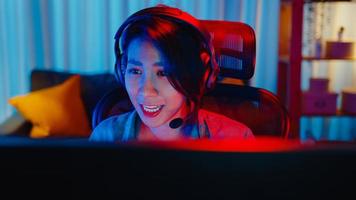 Nahaufnahme Gesicht glücklich Asien professionelles Mädchen Gamer tragen Kopfhörer Wettbewerb Videospiel Neonlicht Computer im Wohnzimmer zu Hause spielen. Esport-Streaming-Spiel online, Heimquarantäne-Aktivitätskonzept. foto