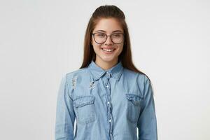 Porträt von sehr süß und attraktiv Mädchen im Brille lächelnd, gekleidet im ein modisch Denim Shirt, isoliert auf ein Weiß Hintergrund foto