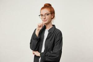 Porträt von jung rot -Haar weiblich im schwarz Herren Shirt, hält Arm auf Kinn und sieht aus hoch, grübelt das Idee, Erwägen anders Varianten, Denken Was tun zu lösen das Problem, Über Weiß Hintergrund foto