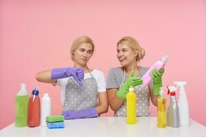 Innen- Schuss von jung weißköpfig Frauen mit beiläufig Frisur gekleidet im Uniform während posieren Über Rosa Hintergrund, vorbereiten zum Frühling Reinigung und wählen Waschmittel foto