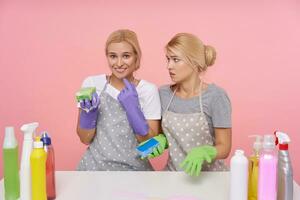 Studio Schuss von jung ziemlich blond Reinigung Damen halten Schwämme im angehoben Hände während Sitzung Über Rosa Hintergrund. Hausarbeit und Hauswirtschaft Konzept foto