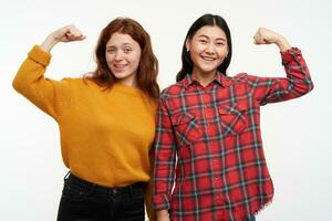 zwei jung, glücklich Frauen Freunde. tragen Gelb Sweatshirt und kariert Shirt. zeigen Wie stark Sie Sind, Muskeln. voll von Energie. Menschen Konzept. Aufpassen beim das Kamera, isoliert Über Weiß Hintergrund foto