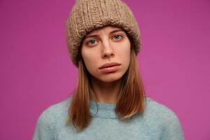 ernst suchen Frau, schön Mädchen mit Brünette Haar. tragen Blau Sweatshirt und gestrickt Hut. warten zum Ihre antworten. Aufpassen beim das Kamera, schließen hoch, isoliert Über lila Hintergrund foto