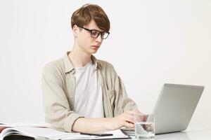 Gefährte Schüler im Brille sitzt beim ein Schreibtisch mit ein Gerade Haltung, konzentriert auf ein Computer, Lernen oder Arbeiten, tippen, Tasten, suchen Information foto
