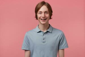 Porträt von nett weit lächelnd blauäugig ordentlich gekämmt jung Kerl mit Hosenträger auf Zähne trägt Polo T-Shirt sieht aus glücklich isoliert Über Rosa Hintergrund foto