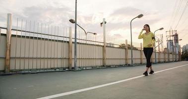 Schöne junge asiatische Sportlerin trainiert mit dem Smartphone, um Musik beim Laufen in der städtischen Umgebung zu hören. koreanisches jugendlich Mädchen, das am frühen Morgen Sportkleidung auf der Gehwegbrücke trägt. foto