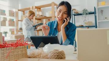 Junge Geschäftsfrauen in Asien, die einen Handyanruf verwenden, erhalten eine Bestellung und überprüfen das Produkt auf Lager im Home Office. Kleinunternehmer, Online-Marktlieferung, Lifestyle-Freelance-Konzept.