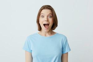 Porträt von überrascht glücklich jung Frau mit geöffnet Mund im Blau t Hemd fühlt sich aufgeregt und schreien isoliert Über Weiß Hintergrund foto