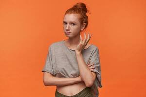 Porträt von attraktiv jung Frau mit foxy Haar im Knoten Stehen Über Orange Hintergrund, suchen zu Kamera verwirrt mit angehoben Palme. Mensch Emotion Gesichts- Ausdruck Körper Sprache foto