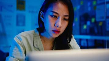 Freiberufliche asiatische Frauen, die harte Arbeit des Laptops im neuen normalen Büro verwenden. Nachtarbeit von zu Hause aus Überlastung, Fernarbeit, Selbstisolation, soziale Distanzierung, Quarantäne zur Vorbeugung von Coronaviren.