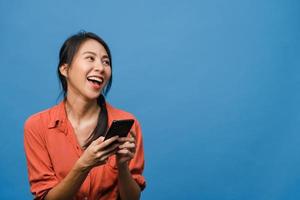 junge asiatische dame, die telefon mit positivem ausdruck verwendet, breit lächelt, in lässiger kleidung gekleidet fühlt sich glücklich und steht einzeln auf blauem hintergrund. glückliche entzückende frohe frau freut sich über erfolg.