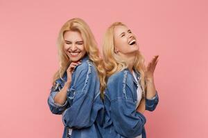 Studio Foto von froh jung lange behaart blond Schwestern Sein im hoch Geist und Lachen glücklich mit geschlossen Augen während Stehen Über Rosa Hintergrund