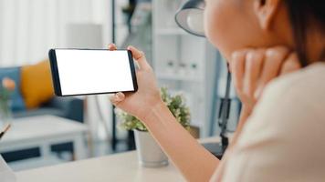 junge asiatische Dame verwendet ein Smartphone mit leerem weißem Bildschirm für Werbetexte, während sie von zu Hause aus im Wohnzimmer arbeitet. Chroma-Key-Technologie, Marketing-Design-Konzept. foto