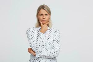 Nahansicht von ernst nachdenklich blond jung Frau trägt Polka Punkt Hemd hält Hände gefaltet, sieht aus nachdenklich und Denken isoliert Über Weiß Hintergrund foto