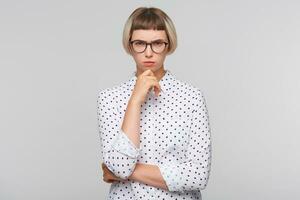 Porträt von nachdenklich ernst blond jung Frau trägt Polka Punkt Hemd und Brille sieht aus konzentriert und wütend isoliert Über Weiß Hintergrund foto