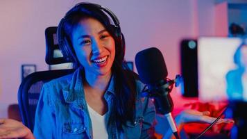 Happy Asia Girl Blogger Music Influencer verwenden Smartphone-Broadcast-Aufnahmen tragen Kopfhörer online Live-Gespräch mit Zuhörern im Wohnzimmer-Heimstudio in der Nacht. Inhaltsersteller-Konzept. foto