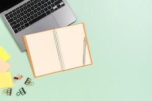 kreatives flaches Laienfoto des Arbeitsplatzschreibtisches. Schreibtisch von oben mit Laptop, Kaffeetasse und offenem schwarzen Notizbuch auf pastellgrünem Hintergrund. Draufsichtmodell mit Kopienraumfotografie.