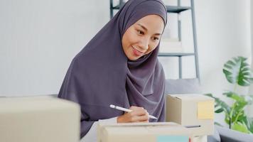 Junge asiatische muslimische Geschäftsfrau Produktbestellung auf Lager überprüfen und auf Tablet-Computerarbeit im Home-Office speichern. Kleinunternehmer, Online-Marktlieferung, Lifestyle-Freelance-Konzept.