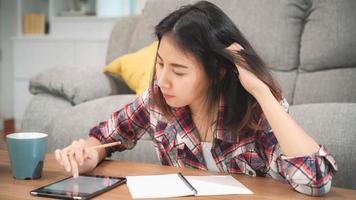 asiatische studentin macht hausaufgaben zu hause, frau trinkt kaffee und verwendet tabletten für die suche auf dem sofa im wohnzimmer zu hause. Lifestyle-Frauen entspannen sich zu Hause Konzept.