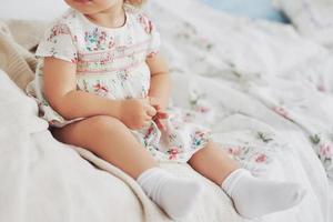 Kindheit Konzept. Babymädchen in süßem Kleid, das im Bett spielt und mit Spielzeug zu Hause spielt. weißes Vintage-Kinderzimmer foto