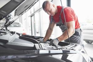 Bild, das einen muskulösen Autoservice-Mitarbeiter zeigt, der das Fahrzeug repariert foto