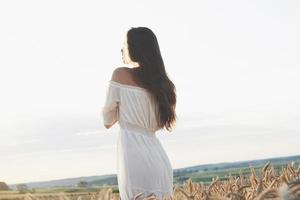 schönes Mädchen im weißen Kleid, das bei Sonnenuntergang auf dem Herbstweizenfeld läuft