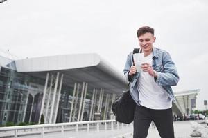 junger gutaussehender mann mit einer tasche auf der schulter in Eile zum Flughafen. foto