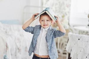 Foto eines fleißigen Schülers mit Buch auf dem Kopf, der Hausaufgaben macht. der schüler hat es satt, hausaufgaben zu machen