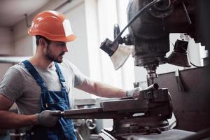 erfahrener Bediener mit Schutzhelm. Konzept der Metallverarbeitungsindustrie Berufsingenieur Metallarbeiter, der CNC-Fräsmaschinenzentrum in der Fertigungswerkstatt betreibt foto