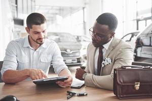Ein junger attraktiver schwarzer Geschäftsmann kauft ein neues Auto, er unterschreibt einen Vertrag und bringt die Schlüssel zum Manager