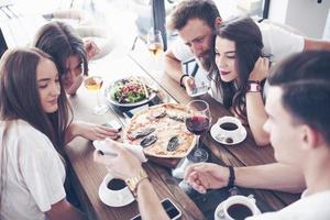 leckere Pizza auf dem Tisch, mit einer Gruppe junger lächelnder Leute, die sich im Pub ausruhen? foto