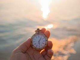 schließen oben von Jahrgang Tasche Uhr im Frau Hand mit Meer im das Sonnenuntergang Zeit wie Hintergrund. foto