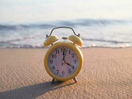 Gelb Alarm Uhr auf das Strand im das Sonnenuntergang Zeit. das Konzept Über Zeit zu Sommer, reisen, Ferien und Entspannung foto