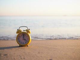 Gelb Alarm Uhr auf das Strand im das Sonnenuntergang Zeit. das Konzept Über Zeit zu Sommer, reisen, Ferien und Entspannung foto