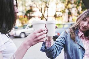 lächelnde Mädchen im Teenageralter mit Kaffeetassen auf der Straße. Getränke und Freundschaftskonzept